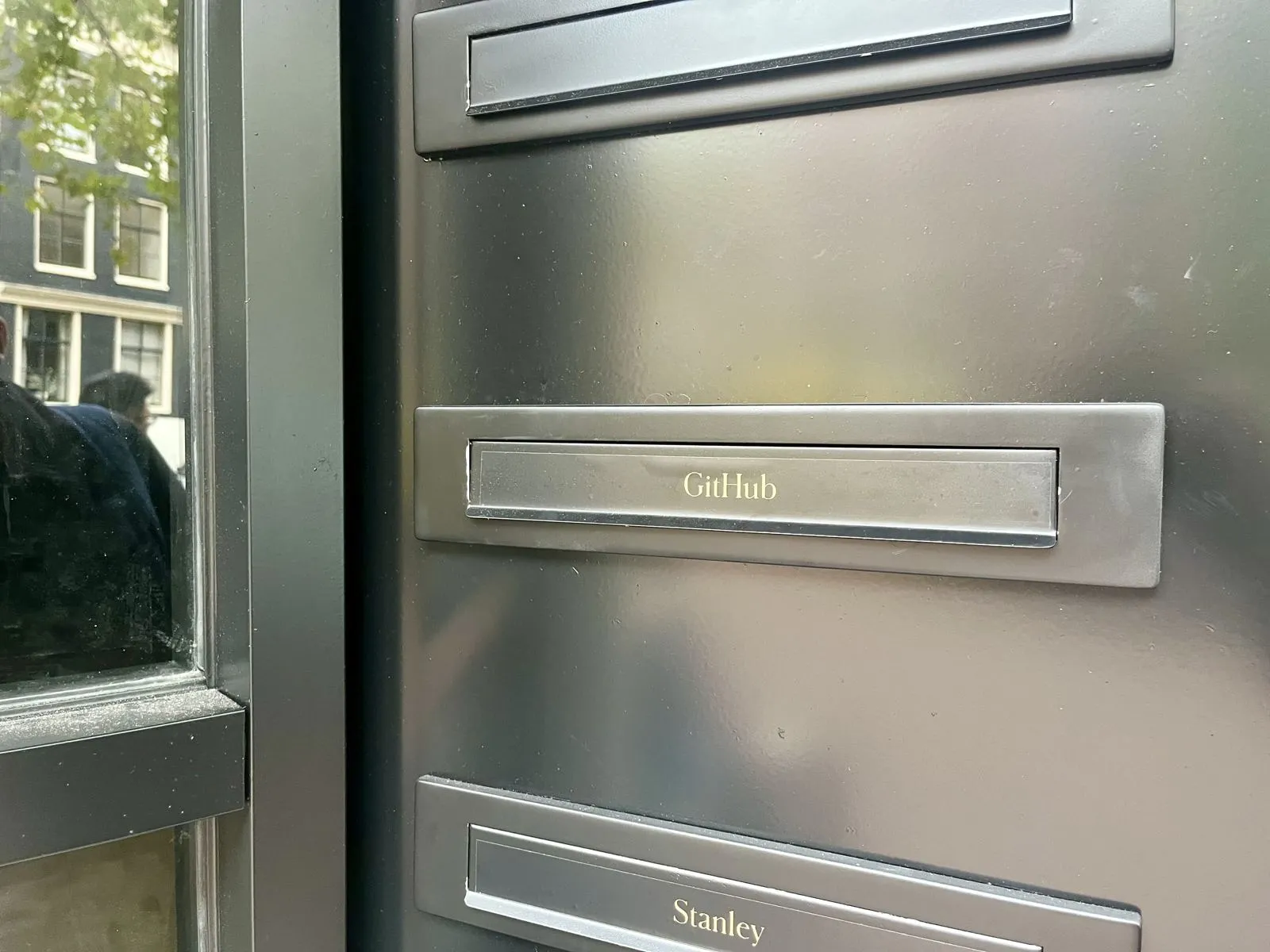 A steel letterbox labelled GitHub on the door of a canal house in Amsterdam, between the boxes of two other tenants